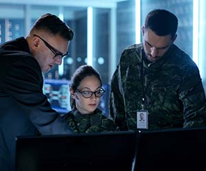 Three military personnel look at a computer screen