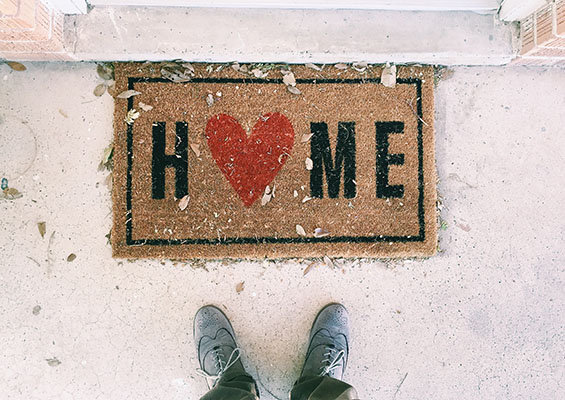 A man stands in front of a door with a welcome mat that says 'Home'