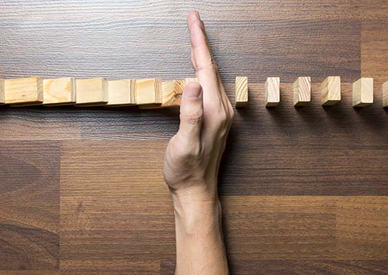 A person puts their hand in a row of dominoes to keep them from falling.